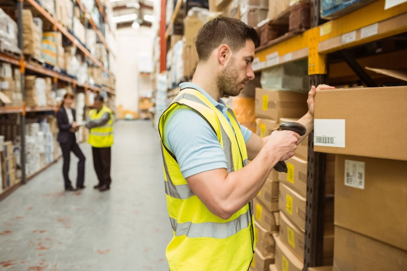 a man scanning boxes in a warehouse while 2 people talk in the background