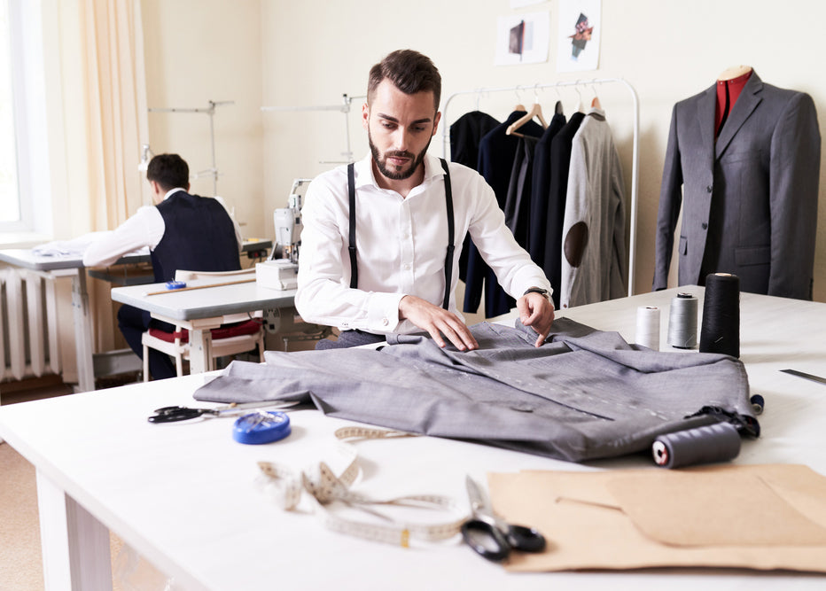 a tailor is working on a suit jacket, with various workroom tools and accessories
